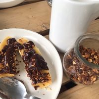 On the left : banana with chocolate sauce and nuts. On the right : homemade granola and plant milk at Joe's Place in Pico
