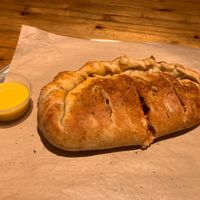 Calzone filled with red sauce, vegan cheese, mushrooms, green bell pepper, red onion and a side of vegan garlic butter at Dells Pizza Lab in Wisconsin Dells