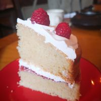 Close up of a slice of Victoria sponge cake on a red plate, sandwiched with vegan creme and jsm, topped with creme and a raspberry at Planetwise & Yoga Studio in Bridlington