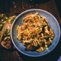 Vegan potato wedges (the crispiest, most delicious ever) smothered in herbs, cashew cheese aoli and crispy fried onions. On the side are fresh tacos with creamy avocado at Teva in Rio De Janeiro