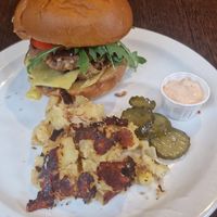 Yelamu: 2 VG sausage patties, brioche bun, smoked vegan Applewood cheese, caramelised onions, fresh tomato, rocket. Served with homemade potato hash, Moose pickles & chipotle mayo. at Moose Coffee in Manchester
