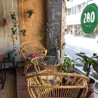 Picture of a glass table and wicker chairs in front of the café’s full-length storefront window. There are plants hanging from a branch in the background, and other plants aroun at OAS Cafe in Kalmar