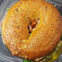 Hendricksons whole grain or sesame bagel sandwich with house lemon basil hummus and layer cucumbers, tomatoes, shredded carrot, home made peppercorn vegan mayo, mustard and a pickle.  at Frickin' Delights Donuts in Devon