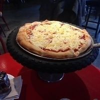 Vegan pizza with DAiya Cheese and pineapple on a serving stand made from a bike wheel at Riders Pizza in Cumberland