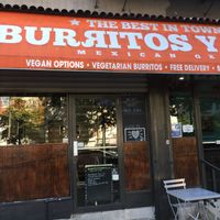 Outside entrance, with simple outdoor seating: notice Happy Cow sticker on front door! at Burritos y Mas in New York City