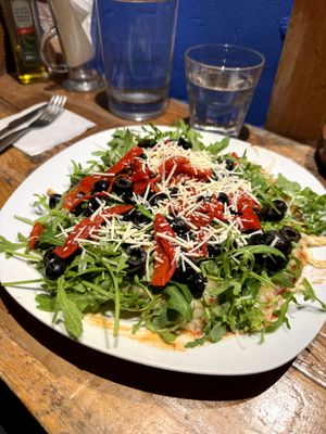 Fainá (pizza base made of chickpea flour), with olives, pepper and rocket leaves at Jardin Urbano in Valencia