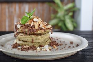 Matcha Nutella Pancakes - Fluffy matcha pancakes stack layered with sliced banana, house-made vegan nutella, toasted coconut flakes & crunchy cacao nibs at Matcha Cafe in Tibubeneng
