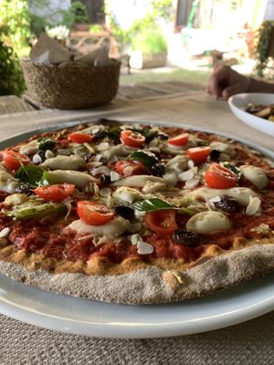Pizza with a dough from wholemeal flour, vegan mozzarella, tomatoes, marinated basil, almonds, zucchini & olives  at Ecosteria Parco Santi Angeli in Santi Angeli