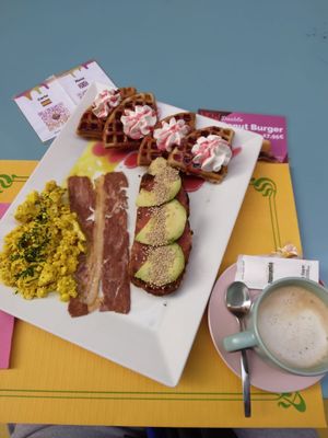Tofu scrambled eggs, avocado toast with a tomato paste, vegan waffles with berries syrup and chantilly, latte with oat milk at Freedom Cakes Bakery in Madrid