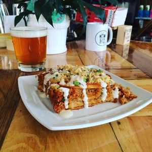 The protein-packed vegan Mexican Lasagna (gluten-free) stacked with corn tortillas, refried beans, quinoa, ground 'beef', red onions, roasted red peppers, purple cabbage, mild jalapeños, and enchilada sauce, topped with hemp hearts, cashew mozzarella, & garlic aioli! at Two Dollar Radio Headquarters in Columbus