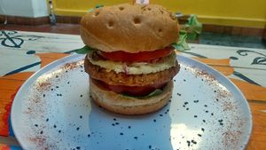 Broaster - (Pan Artesanal de orégano, espinaca, Tomate, hamburguesa apanada de garbanzo, humus cheese, queso cheddar vegano y ripio nacho de maíz) at Vegan Cocina Viva Cali in Cali