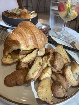 Sausage/cheese/hash brown on a croissant. Mashed potato/“beef” dish in back  at L'Artisane Creative Bakery in Coral Gables