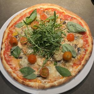 Pizza Sebastian with tomato sauce, vegan cheese, mushrooms, potatoes, basil, salad rocket, and chili oil.  at Café Piccolina in Aarhus