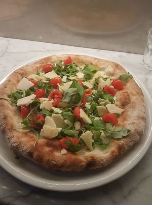 Organic pizza with fresh cherry tomatoes, rocket salad and Parmesan cheese or vegan cheese at La Pepiniere in Florence