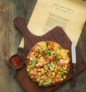 Ragi Pizza- Thin crust ragi pizza  topped with sundried tomato pesto sauce,mozzarella cheese,peppers,cherry tomato,sweet corn, pickled jalapeno and caramelized onion. at Go Native - Jayanagar in Bangalore