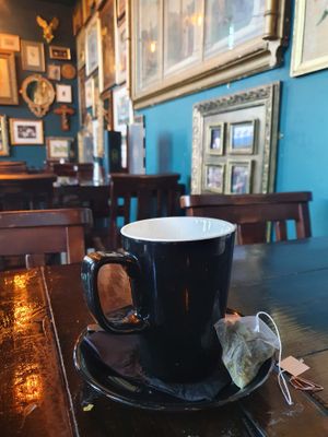 Cup of tea with picture frames in the background. These are filled with Christian iconography. at Church - Temple of Fun in Sheffield