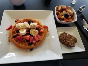 Vegan waffle with blueberries, strawberries, and bananas. Plant based sausage and home fries at Waffles INCaffeinated in Beaver