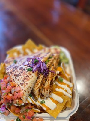Nach-adilla from our Nach-Section. Quesadilla served over corn chips, beans and jalapeño slices, drizzled with crema & queso fundido. Plated with pico de gallo & guacamole. at Luna Verde Vegan Mexican Restaurant in Bradley Beach
