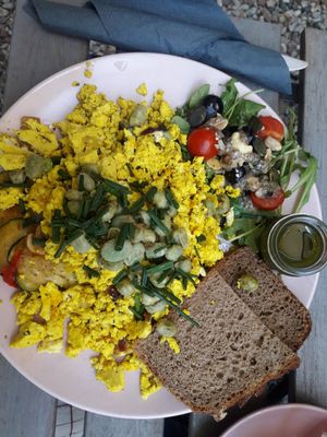 garlic scrambled tofu with pesto, cherry tomatoes, zucchini, mushrooms, sunflower seeds and bread at co Jak co in Poznan