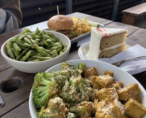 The broccoli tofu and peanut sauce bowl, edamame, burger and kettle chips, and a slice of cake  at The Bye and Bye in Portland