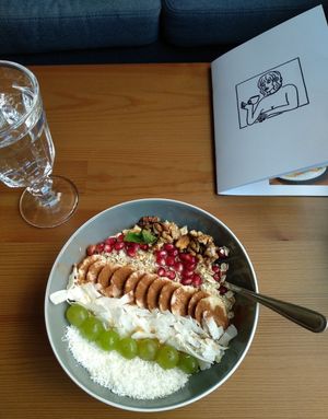 Coconut yoghurt breakfast bowl with banana, coconut, oats, grapes, pomegranate seeds, nuts and maple syrup. at Panenská Kaviareň in Bratislava