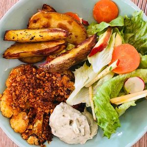 Tranche de chou-fleur panée aux noix de cajou et épices. Servie avec une sauce tartare et accompagnée de salade et de pommes de terre rôties. 
 at Be Kind Cafe in Geneva