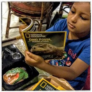 Young paleontologist Kojagori with dino books and fossils (Mosasaur tooth, Dino bone and Dino poop) at First Flush in Kolkata