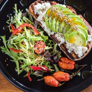 Open sandwich / toasted homemade sourdough
bread. avocado, cherrv tomatoes, sesame seeds
and side green salad with homemade mustard sauce. at Karma in Santorini
