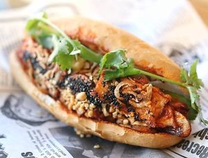 Gochujang braised tofu mushroom banh mi with creamy vegan garlic coleslaw, tangy-sweet daikon, cucumbers, and garnished with black sesame, fried shallots, peanuts, and cilantro. at Rustle & Still in Toronto