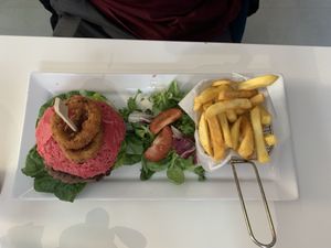 Cheese burger with bacon served on a beetroot bun and a side of chips, salad and onion rings  at Naked Bakery in Edinburgh