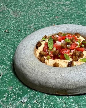 Nattō hummus and salad with greens, tomatoes, and onions, oil with coriander seeds and rye bread croutons with sumac at Veganika in Ljubljana