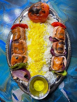 Double Sword Shish Kabob style skewers made with charbroiled Smoked Bacon wrapped Beyond Sausages, grilled bell peppers and onions over Persian style basmati rice and grilled tomato with side of house made garlic butter. at Pythagoras Conscious Food Philosophy in Houston