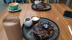 Blueberry buckwheat pancakes with whipped coconut cream and maple syrup, peanut butter cacao smoothie on the left  at Boneless Vegetarian Cafe in Bermagui