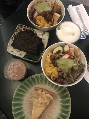 Two small bowls, matcha latte (top right), chai latte (bottom left), black sesame cake, and passion fruit and almond cake  at Tushita in Munich