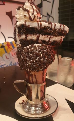 BLACK ‘N WHITE CAKESHAKE CHOCOLATE SHAKE: Vanilla frosted rim with mini chocolate chips topped with a black ‘n white cake slice, whipped cream & chocolate drizzle (AVAILABLE VE at Venetian Hotel - Black Tap in Las Vegas