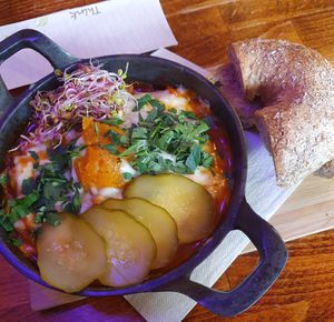 Shakshouka with baked pumpkin "egg", vegan cheese, pickled cucumber, sprouts, and garlic bread at Avocado Spot in Gdansk
