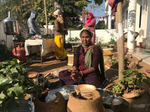 Prakashi ji in the open kitchen making rotis on wood fired chulha.  at AhimsaGram in Jaipur