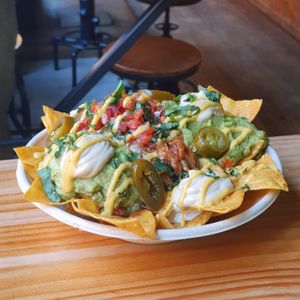 NACHOS DEFINITIVOS: Homemade tortilla chips with refried beans, pulled pork, smashed avocado, pico de gallo, jalapeños, sour cream and cheddar sauce. Ideal to share. at Frutas Prohibidas in Madrid