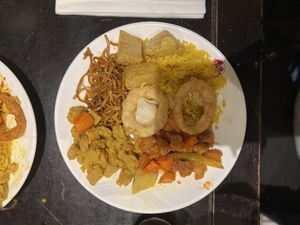 Platter of noodles, fried rice, crispy potatoes, chicken curry, sweet & sour chicken, mixed vegetables and onion rings at Su Vegan Buffet in West London