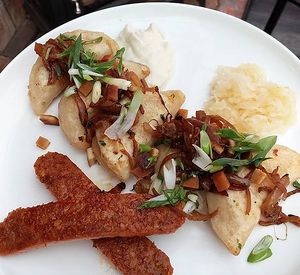 hand-pinched garlic cheddar stuffed perogies with sauteed onions, tofu bacon, beyond bratwurst, raw organic sauerkraut, and blue cheeze aioli at Vegan Street in Calgary