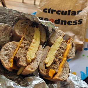 The Basic (Build Your Own Egg Sandwich!) with Blueberry (v) bagel, Toasted, Vegan Egg, Vegan Cheddar, +Vegan Sausage. Pre-cut in half. 😊 at Seize the Bagel in Vancouver