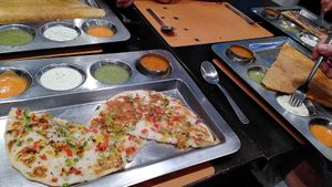 Mixed vegetable uthappam in foreground surrounded by two dosa and one invisible thali at Krishna Vilas in Eindhoven