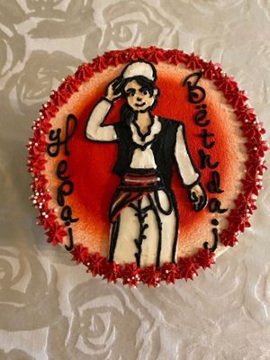 Top of cake features a woman dressed in men’s traditional Albanian costume, with happy birthday intentionally spelled wrong.  at Cakerino in Troy