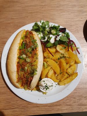 Hotdog bun filled with minced meat in dill sauce, melted cheddar, pickles, caramelized onions and side of roasted
potatoes and salad with ranch sauce at Lucifer Lives in Brussels