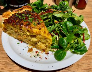 Quiche with cauliflower, caramelized onions en vegan bacon, served with a green salad € 12 (January 2026) at Lucifer Lives in Brussels