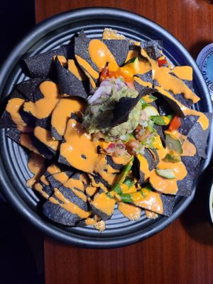 Nachos - Looks good. Tastes terrible. The "cheese sauce" is like orange oil. They have no beans except edamame which I ordered separately. It's mainly chips and oily orange sauce. at The Honu in Dunedin
