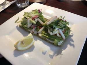 Raw Avo-wild greens sandwich : home made raw coconut bread, avocado, raw almond hummus and raw pesto. Fresh tomatoes and raw Ali-oli with mixed greens, onions, radish and sprouts   at Caravan of Dreams in New York City