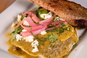 Tostada con huevos with green tomato poblano sauce, crispy corn tortilla, refried beans, house queso, and pickled onions. Make it vegan with tofu scramble and almond ricotta.  at Buena Onda Cafe in St Augustine