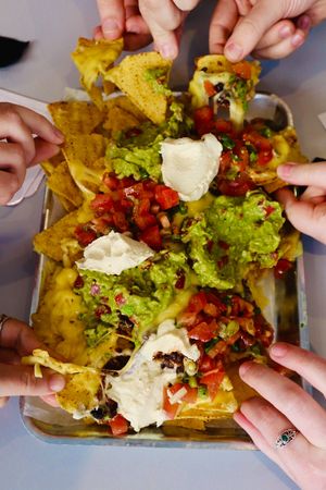 Sharing nachos topped with spiced
black beans, guacamole, salsa, cheese + sour cream at Slice + Dice in Norwich