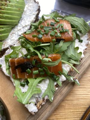 A slice of multi grain seed bread with white bean feta spread, rocket and marinated salmon  at Froindlichst in Berlin